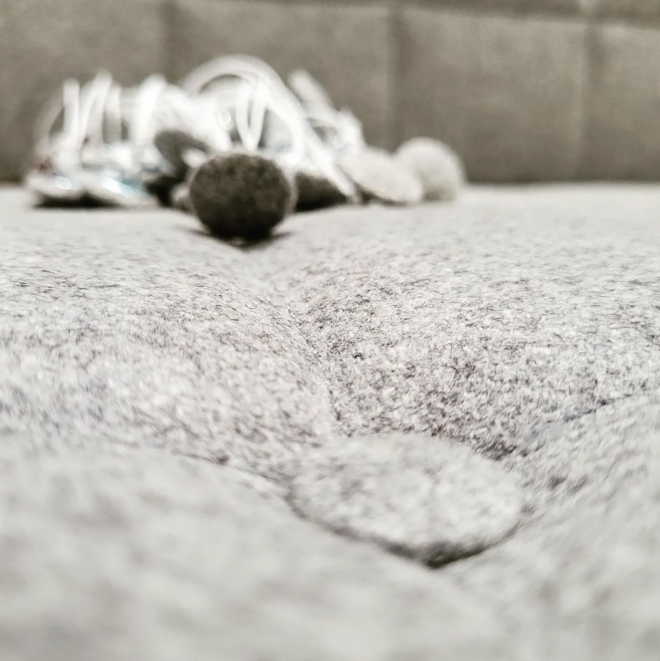 Detailaufnahme einer grauen, textilen Polsterfläche mit Knopfheftung.